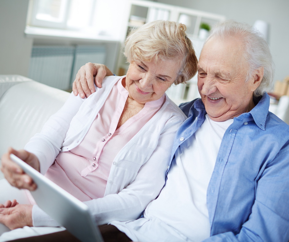 Bild eines Seniorenpaars, das auf einer Couch sitzt und gemeinsam auf einen Tablet-PC schaut.